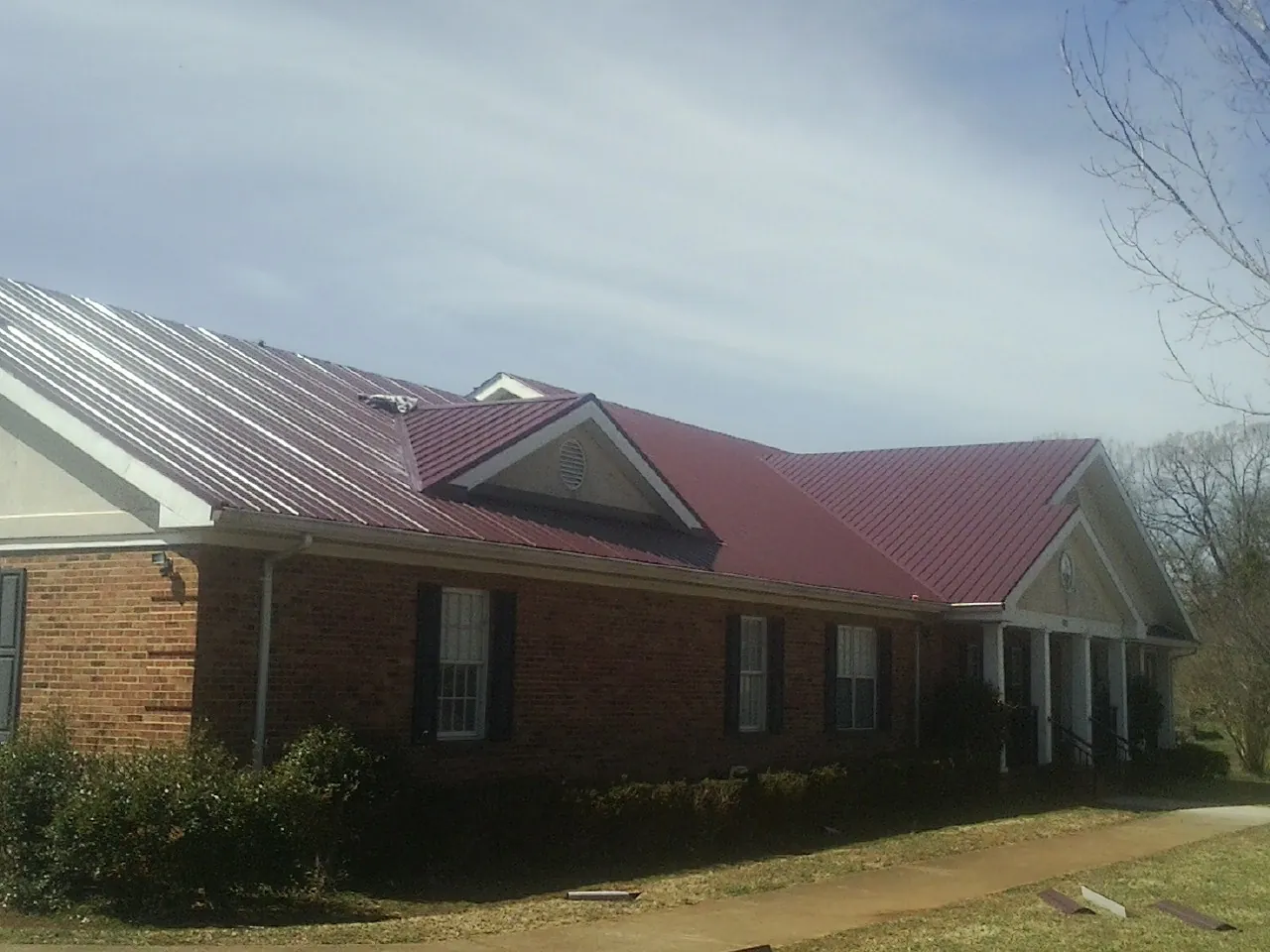Red metal roof with gabled entries on a long brick building, from a Hail Damage Roof Repair job in Delaware City