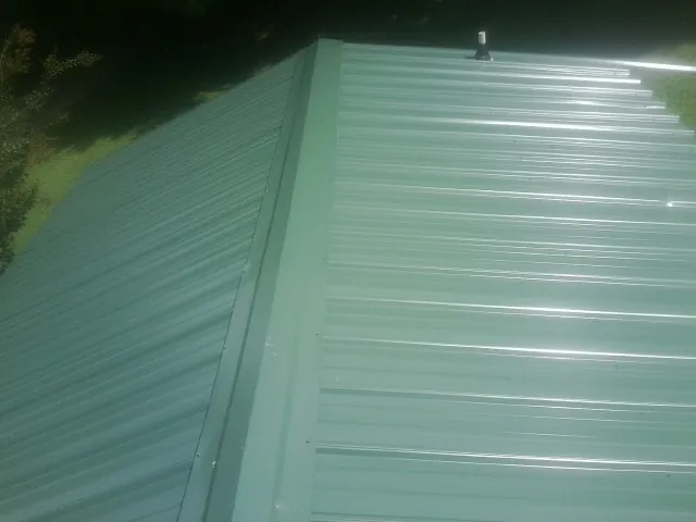 New green metal panels meeting at the ridge of a roof — Flat Roof Repair work by our crew in Delaware City